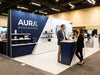 A well-designed 10x10 trade show booth with a bold backwall display and two professionals engaging with visitors in a bright convention hall.