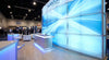 A glowing backlit SEG fabric display wall inside a modern trade show booth, illuminated by cool white light against a blurred convention hall background.