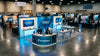 A fully assembled, professional trade show booth with backlit displays and branded counter stands ready in a bright convention hall.